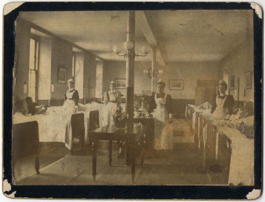4名护士站在医院病房两排病床旁的黑白照片。